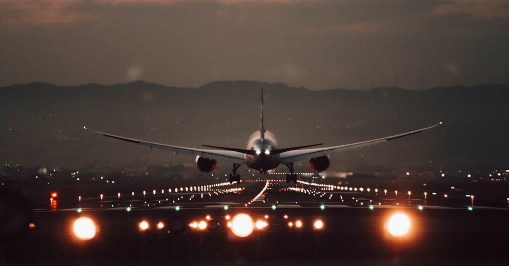 A large airplane makes a dramatic landing on a lit runway at twilight with a scenic mountain backdrop.