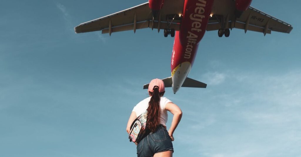 A woman standing on a Phuket beach watches a flying jet overhead, under a clear blue sky.